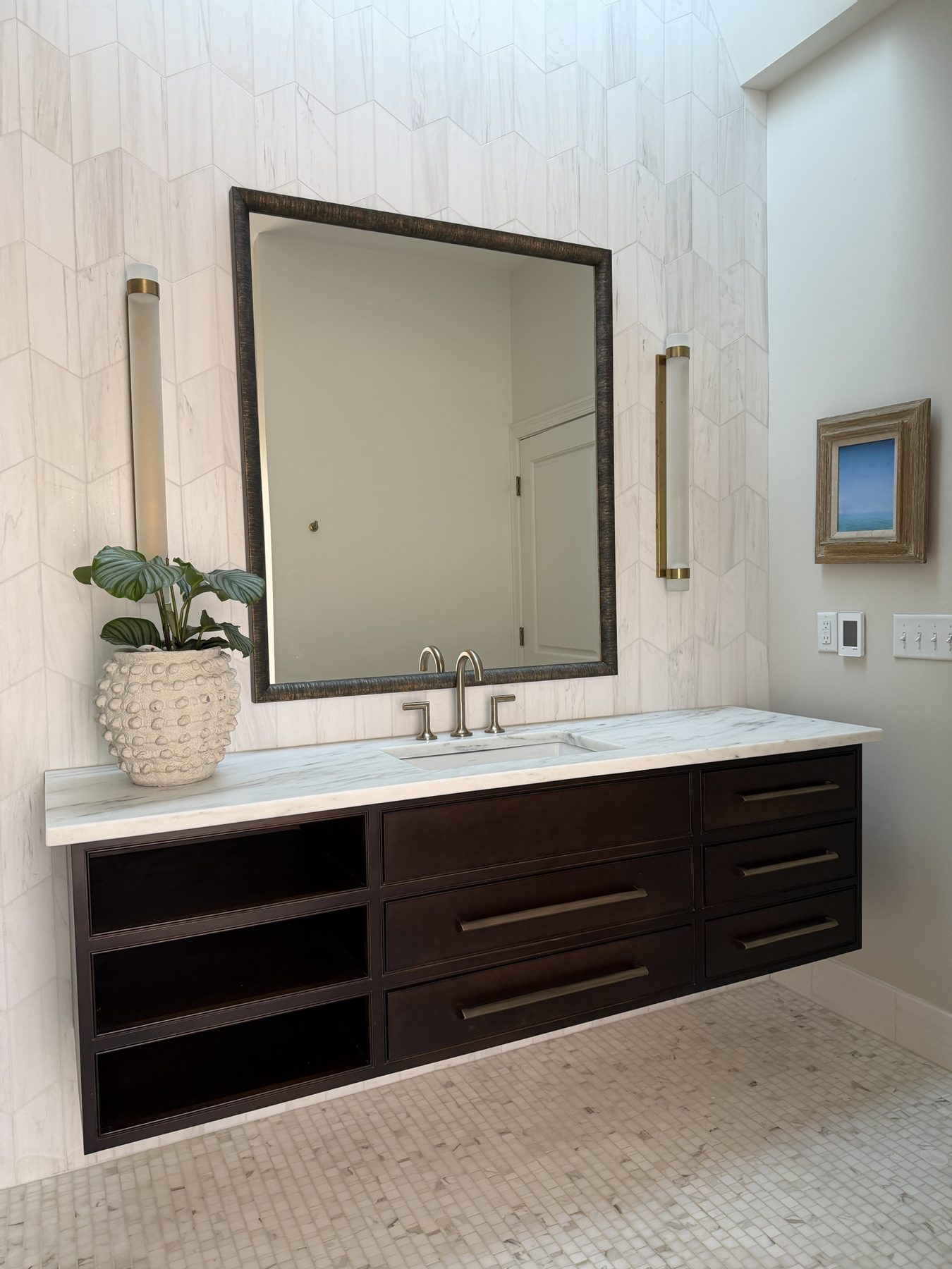 Floating dark-stained vanity with a marble top against chevron tile