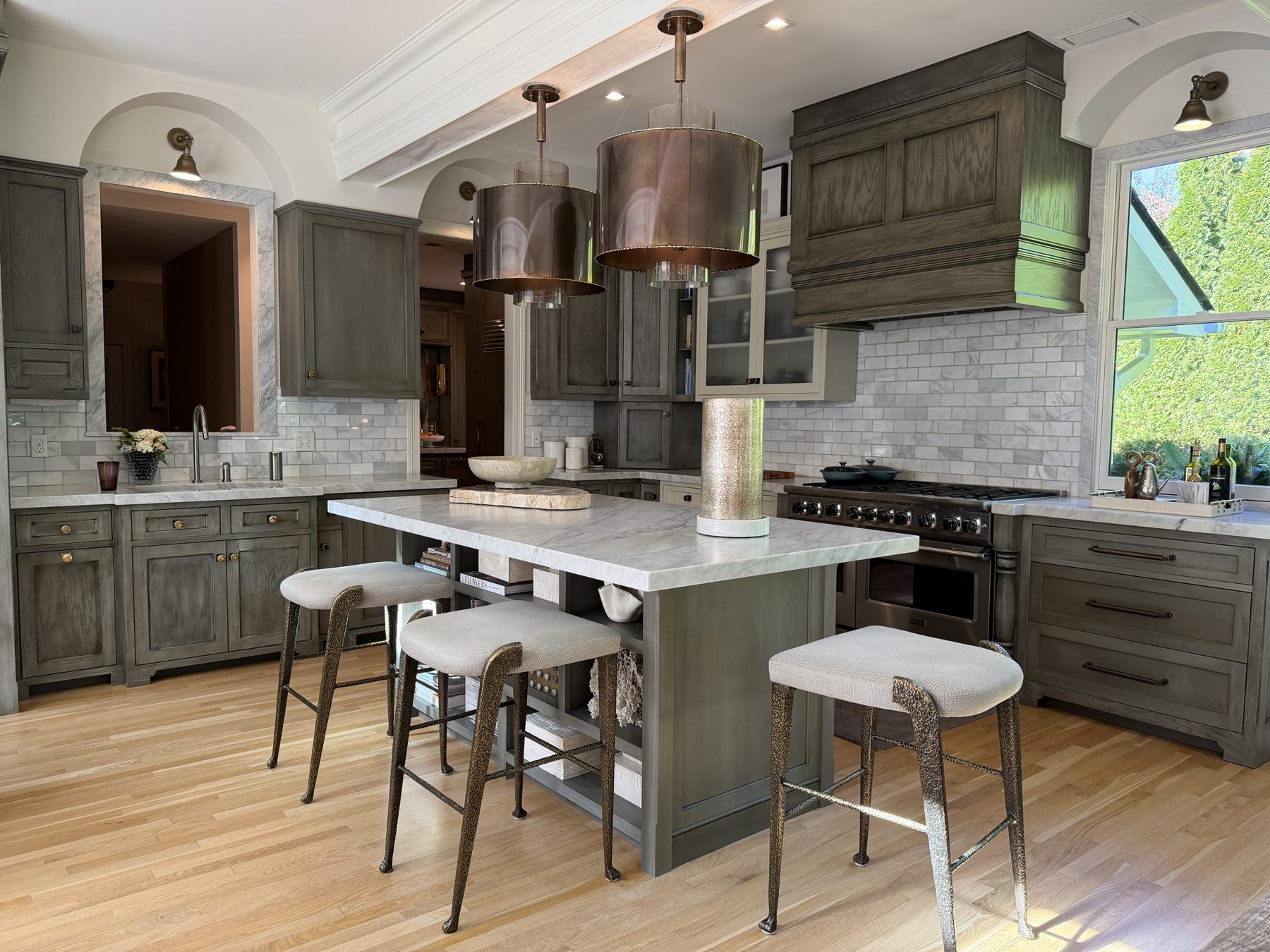 Grey-stained oak kitchen with a marble island, copper pendants, a panelled range hood and arched niches